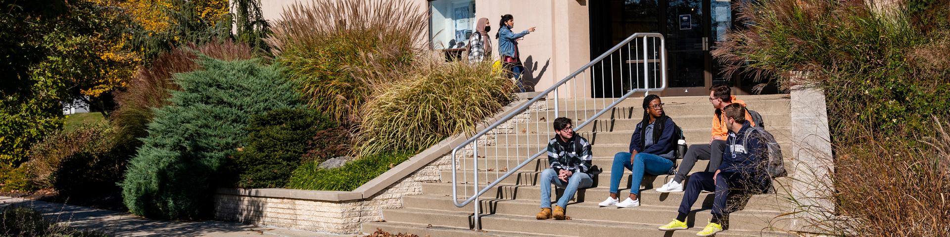 Four students sit and talk on concrete stairs outside of Hintz Bookstore