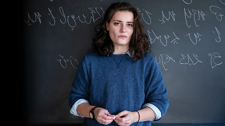 Jannah Martin stands in front of a chalkboard with her constructed language, KFZ, written behind her in chalk.